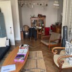 Spacious living and dining room with wooden floors, sofa and armchairs in a host family apartment in central Lyon.