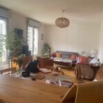 Bright and welcoming living room in a Lyon host family apartment, with large windows, plants and a comfortable dining area.